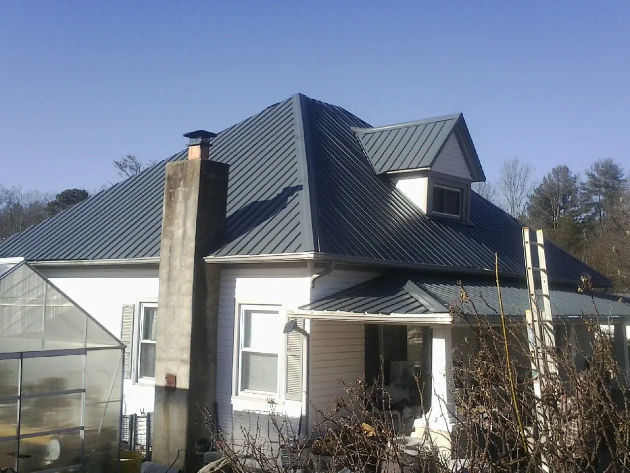 Dark blue standing seam metal roof on a white farmhouse with dormer — Slate & Tile Roof Repair by Roofing Brothers in Lawn