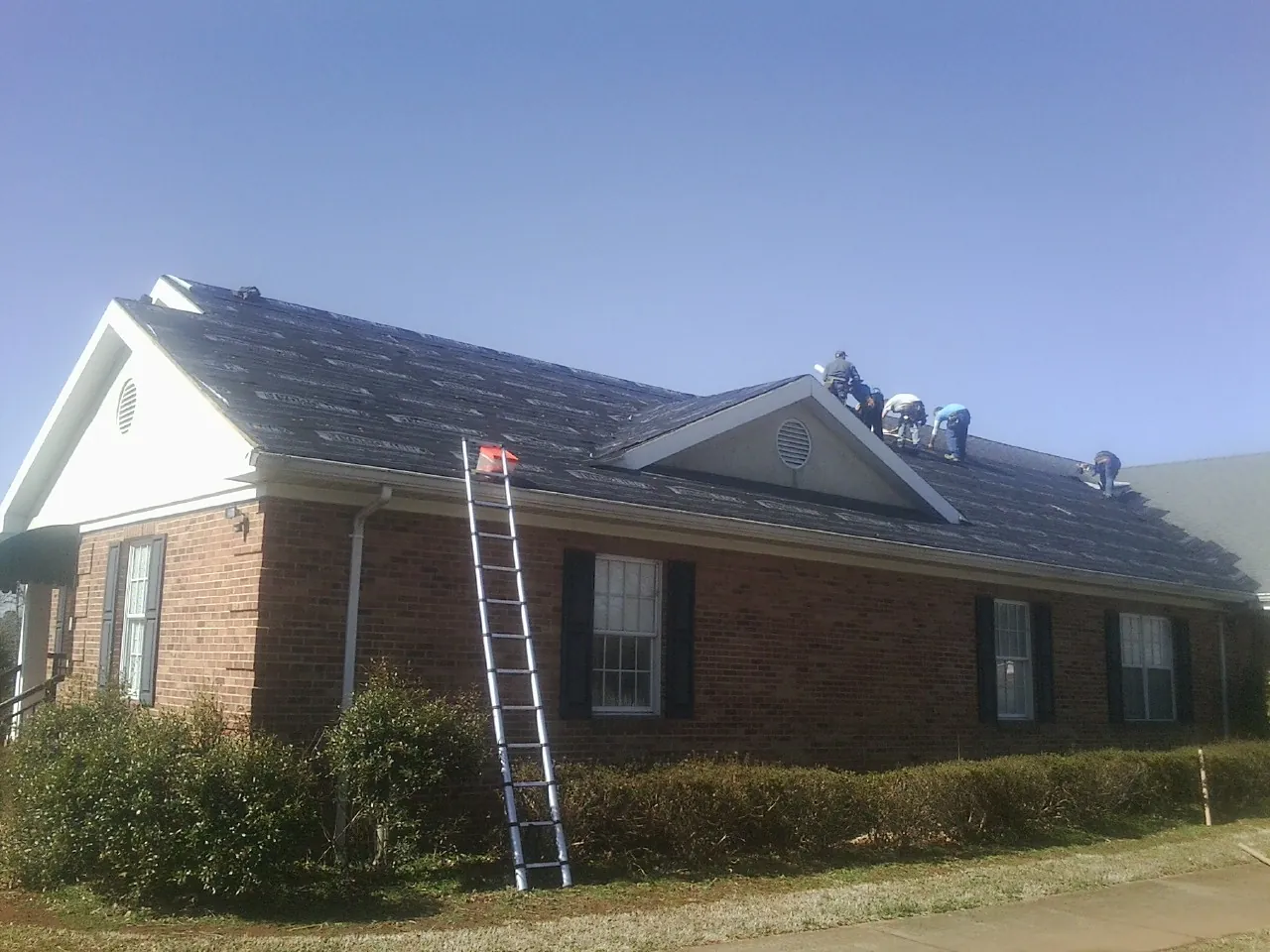 Crew tearing shingles off a brick ranch roof with a ladder set — Metal Roof Repair work by our crew in Lawn