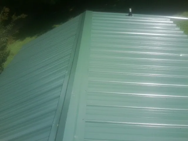 New green metal panels meeting at the ridge of a roof — Flat Roof Repair work by our crew in Lawn