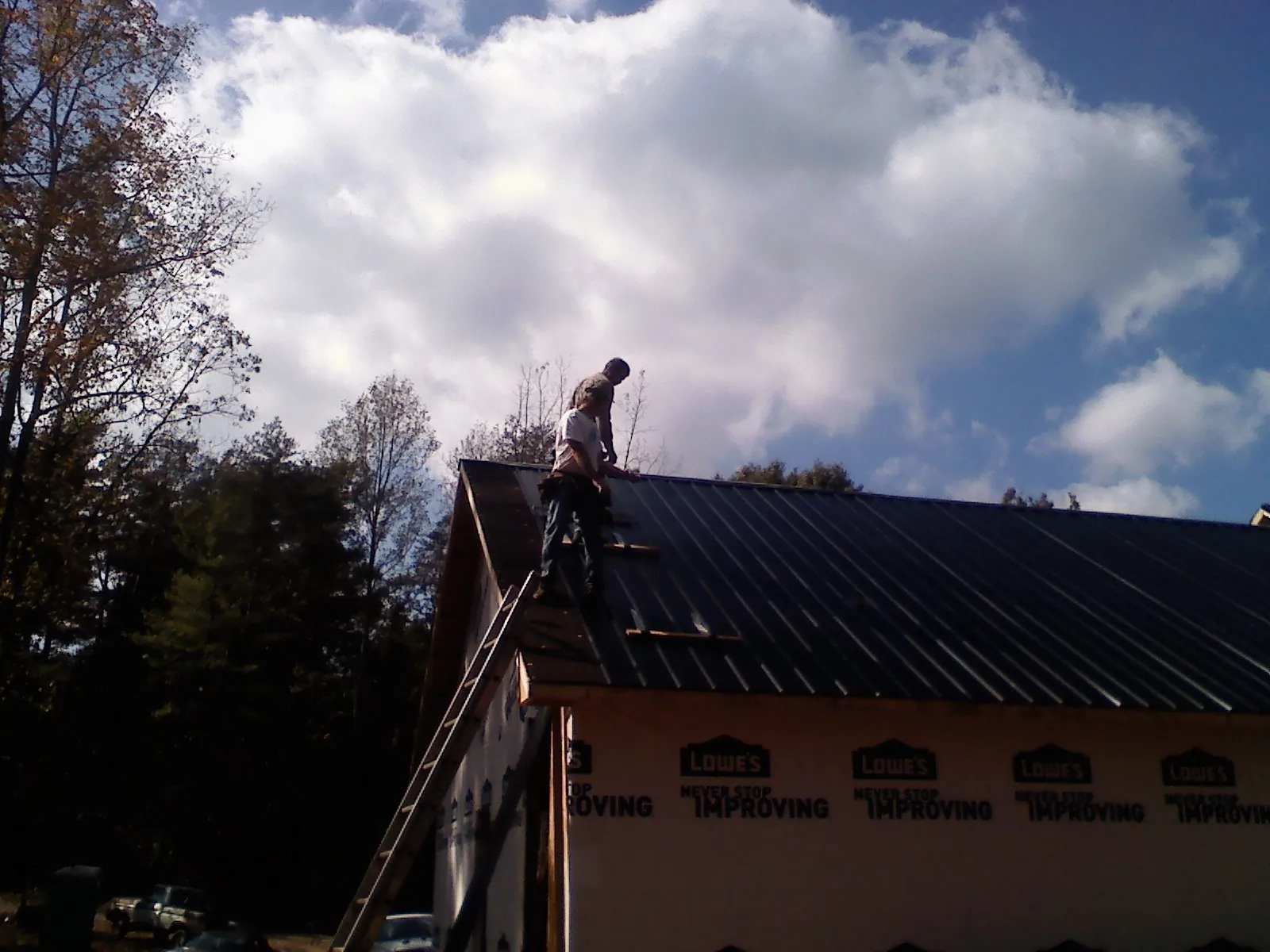 Roofer fastening dark metal panels high against a cloudy sky, from a Roof Inspection job in Lawn