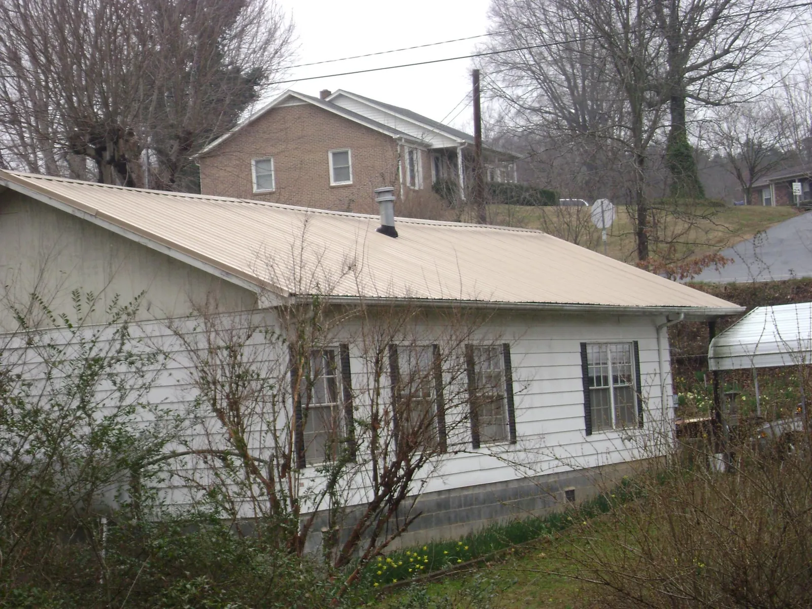 Tan metal roof on a white sided house set into a hillside — Commercial Roofing by Roofing Brothers in Lawn